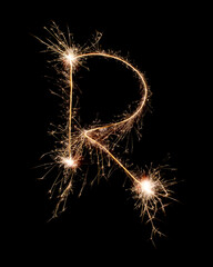 Sparkling burning creative letter R isolated on black background. Beautiful glowing golden overlay object for design holiday greeting card. Creative lettering R written with burning sparklers