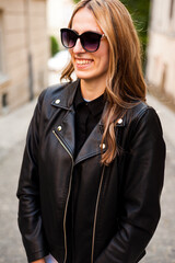 Smiling woman in the city street wearing black leather jacket and white pants and sunglasses