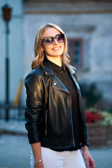 Smiling woman in the city street wearing black leather jacket and white pants and sunglasses