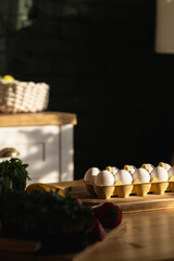 White eggs in a yellow egg box on a wooden board lying on a wooden table. Kitchen background. Emphasis on eggs.
