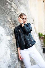 Smiling woman in the city street wearing black leather jacket and white pants and sunglasses