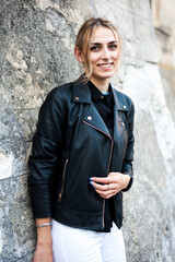 Smiling woman in the city street wearing black leather jacket and white pants and sunglasses