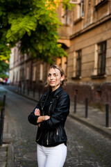 Fototapeta premium Smiling woman in the city street wearing black leather jacket and white pants and sunglasses