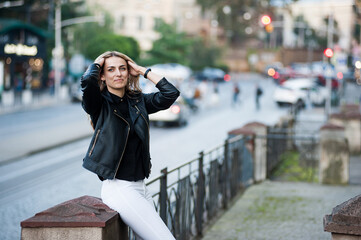Smiling woman in the city street wearing black leather jacket and white pants and sunglasses