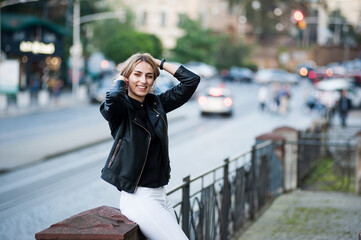 Smiling woman in the city street wearing black leather jacket and white pants and sunglasses