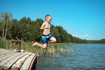 cute caucasian boy jumping from wooden pier diving into lake in countryside