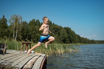 Fototapeta na wymiar cute caucasian boy jumping from wooden pier diving into lake in countryside