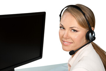 Portrait of beautiful young woman with headset sitting near pc and looking at camera on a white...