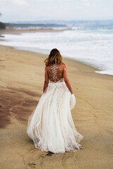 Fototapeta na wymiar Back view of a bride in a white wedding dress on the beach