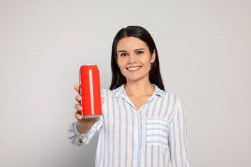 Beautiful young woman holding tin can with beverage on light grey background