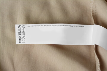 White clothing label with care information on beige garment, top view