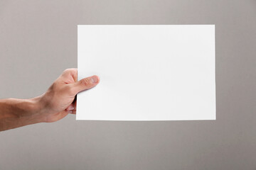 Man holding sheet of paper on grey background, closeup. Mockup for design