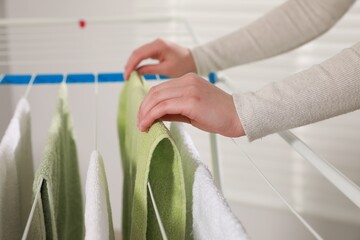Woman hanging clean terry towels on drying rack indoors, closeup