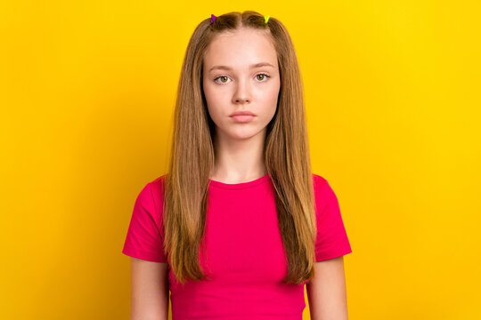 Photo of serious confident schoolgirl with straight hairstyle wear pink t-shirt looking at camera isolated on yellow color background