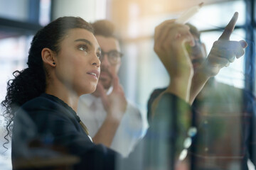 Succeeding is top priority. Shot of a group of colleagues brainstorming together on a glass wall in...