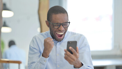 Obraz na płótnie Canvas Portrait of African Man Celebrating on Smartphone