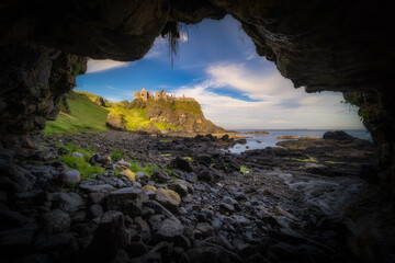 Dunluce Castle seen from a small cave on a shoreline, nested on the edge of cliff, part of Wild...