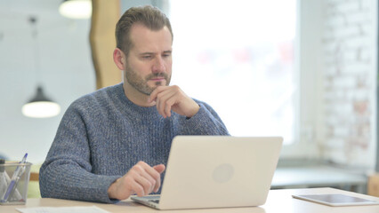 Middle Aged Man Thinking while Working on Laptop