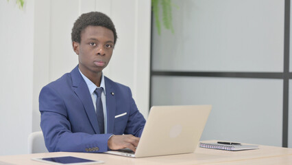 Fototapeta premium African Businessman Looking at Camera while using Laptop