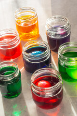 Dyeing Easter Eggs in Colorful Dye in Glass Jars on Marble Counter