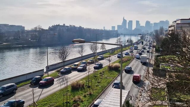 Busy traffic on highway and city streets creating high pollution and smog. Urban view across Seine river to La Defense metropolitan district, Paris, France