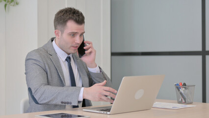 Fototapeta premium Displeased Young Businessman Talking Angrily on Smartphone at Work