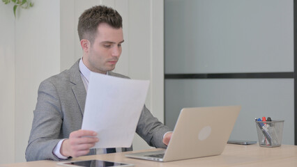 Obraz premium Young Businessman Working on Laptop and Documents