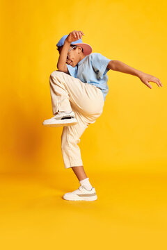 Dynamic portrait of little african boy, hip-hop dancer in stylish street style clothes dancing over bright yellow background. Concept of music, dance happiness