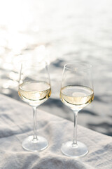 Two glasses of white wine and a wooden plate with bread and olives on a pier at sunset. - obrazy, fototapety, plakaty