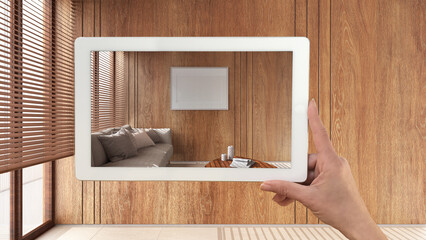 Augmented reality concept. Hand holding tablet with AR application used to simulate furniture and design products in empty wooden interior with marble floor, japandi living room