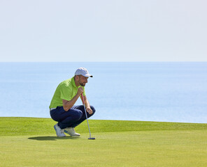 Golfer on the green overlooking the ocean, with a putter in his hands. the player on the green evaluates the slopes and the distance to the hole before aiming the ball at the flag.