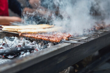 Delicious Adana kebabs are grilling on a barbecue with smoke, close up