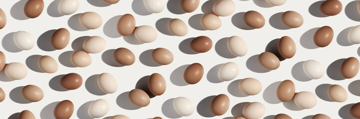 Natural Easter eggs trend pattern white background, shadow at sunlight. Chicken eggs with pastel beige gradient color eggshells, holiday food Easter banner, top view, aesthetic flat lay minimal