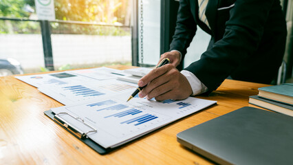 Businessman hand holding a pen pointing in document, financial graph, plan, marketing graph. Financial investment and business strategy data chart report and working on laptop in office