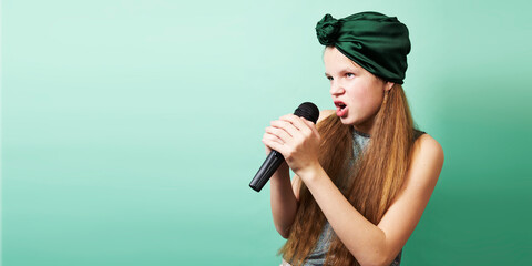 A teenage girl in a green turban holds a microphone in her hands and sings a song. Studio portrait on a green background.