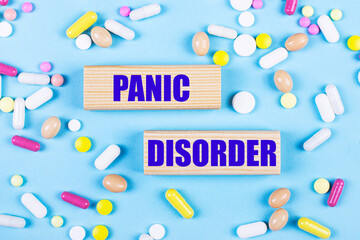 On a light blue background, multi-colored pills and wooden blocks with the text PANIC DISORDER. Pharmaceutics. Medical concept.