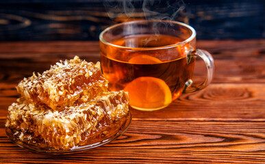 honey in honeycombs and a mug of tea on a brown wooden background