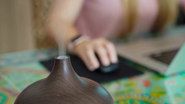 The video features a young woman sitting at a desk in her apartment, working on her laptop. A working electric aromatherapy diffuser is seen to the side of her, emitting a soothing fragrance. The