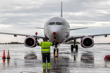 Airplane marshalling at the aiport apron in rainy weather. Passenger aircraft meeting