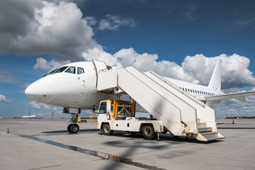 Fototapeta na wymiar White passenger jetliner with air-stairs on the airport apron