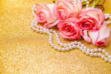Pink rose and pearl necklace on a shiny gold background
