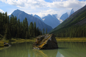 Picturesque landscape with mountains and a greater stone in middle of a green smooth surface of water