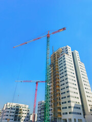 Fototapeta na wymiar Construction of houses in Israel 2023. Two cranes next to boxes of houses, against a clear sky