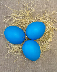 Blue Easter eggs lie in straw on a linen tablecloth. Easter religion concept.