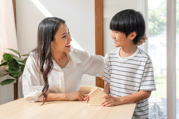 Asian mother looking her son saving money put coins into home bank model at home