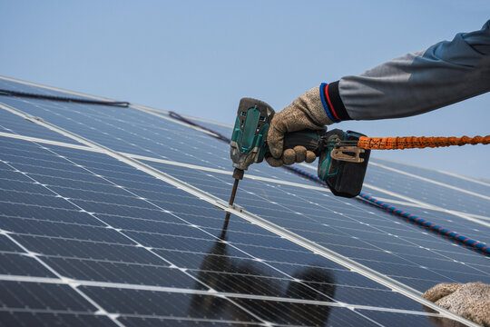 The Technician Is Drilling Holes To Mount The Solar Panel Cell With Electric Drill On Top Of The Roof.