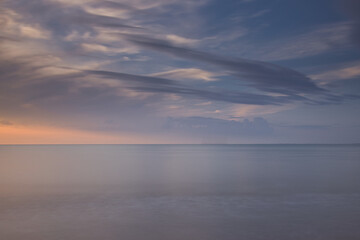 Horizontal view on the sea with calm water. North sea during sunset with dramatic dark clouds at the sky. Seascape with copy space and long exposure
