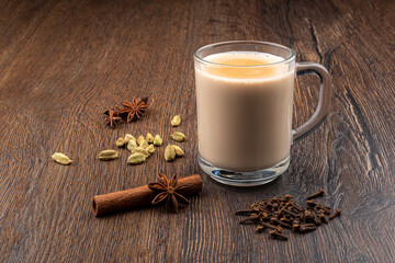 Fototapeta na wymiar Glass mug with masala tea and spices of cloves, cardamom, cinnamon with star anise on a wooden background.