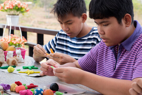 Asian boys spending free time with modeling clays at home by molding plasticine into the shapes of animals, fruits and other things at home, in motion.