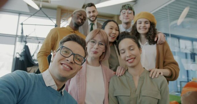 POV portrait of joyful coworkers diverse group taking selfie in creative office smiling looking at camera. Youth and photography concept.
